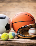 A soccer ball, basketball, tennis balls, and a baseball glove with a baseball on a wooden surface.
