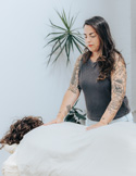 A tattooed practitioner places her hands on the back of a client lying face down on a massage table.