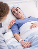 Woman lying in a hospital bed receiving supportive care from a caregiver.