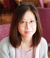 Closeup of young woman with dark hair and eyeglasses wearing mauve shirt with white sweater.