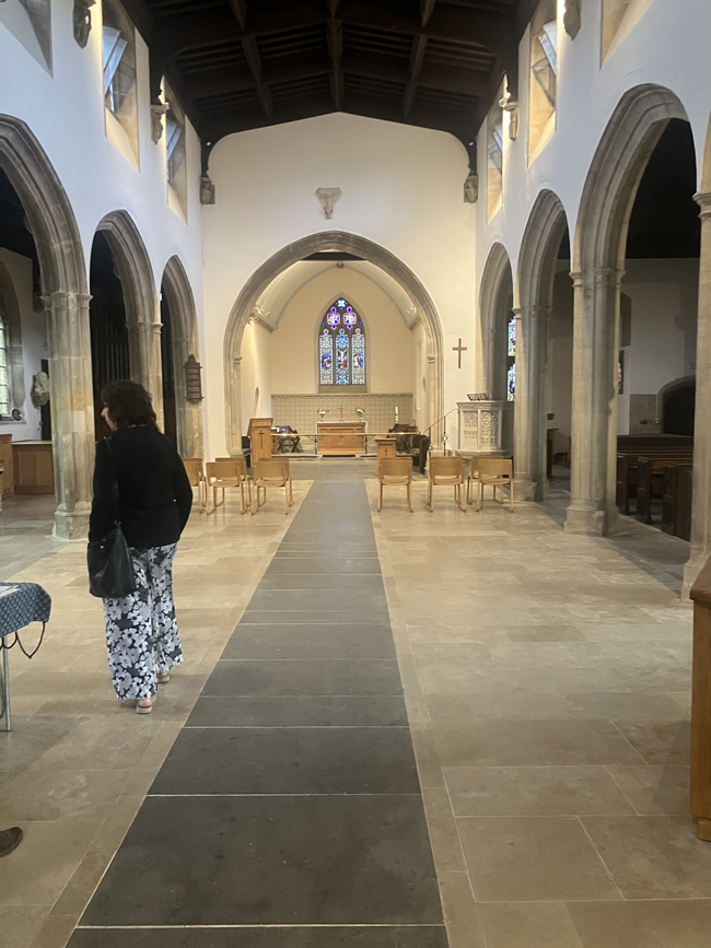 Interior of a historic stone church with arched columns, stained glass, altar, and a central aisle.