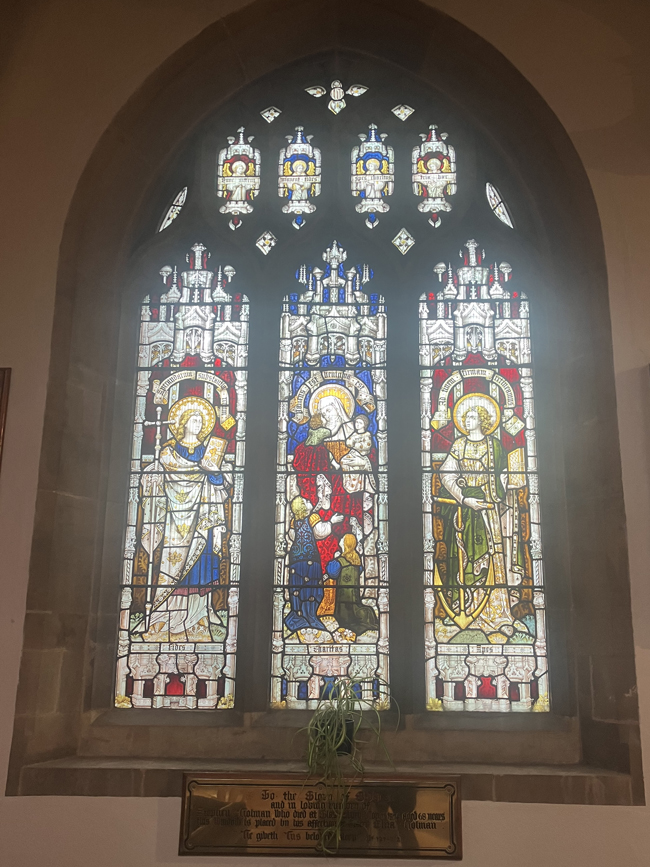 Stained-glass church window depicting three religious figures in ornate medieval-style panels.