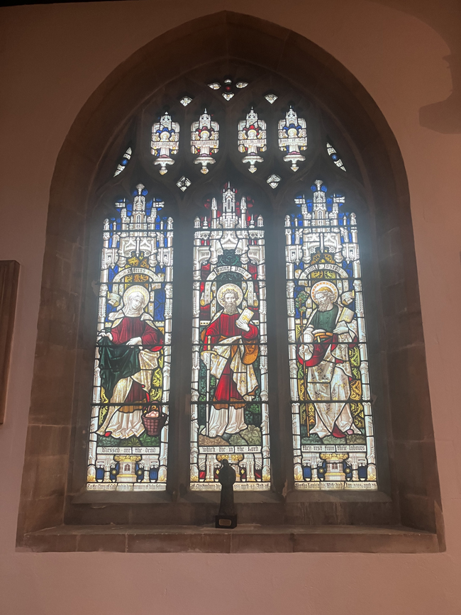 Stained-glass church window depicting three biblical figures in ornate Gothic-style panels.