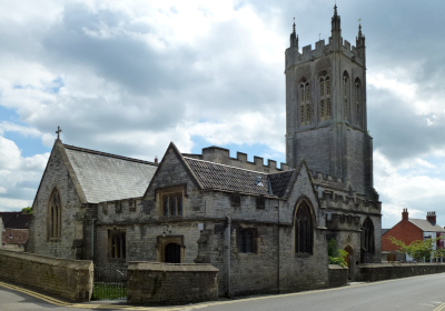 Stone church tower with Gothic arched windows, set against a partially cloudy sky.