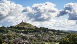 View of Glastonbury Tor on Summer day with partially blue sky and puffy clouds in the background.