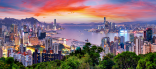 Vibrant panoramic view of Hong Kong’s skyline at sunset, with skyscrapers, Victoria Harbour, and lush foreground greenery.